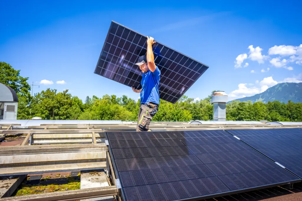 Monteur der Sonnen-Energie beim Transport eines Solarmoduls aufs Dach